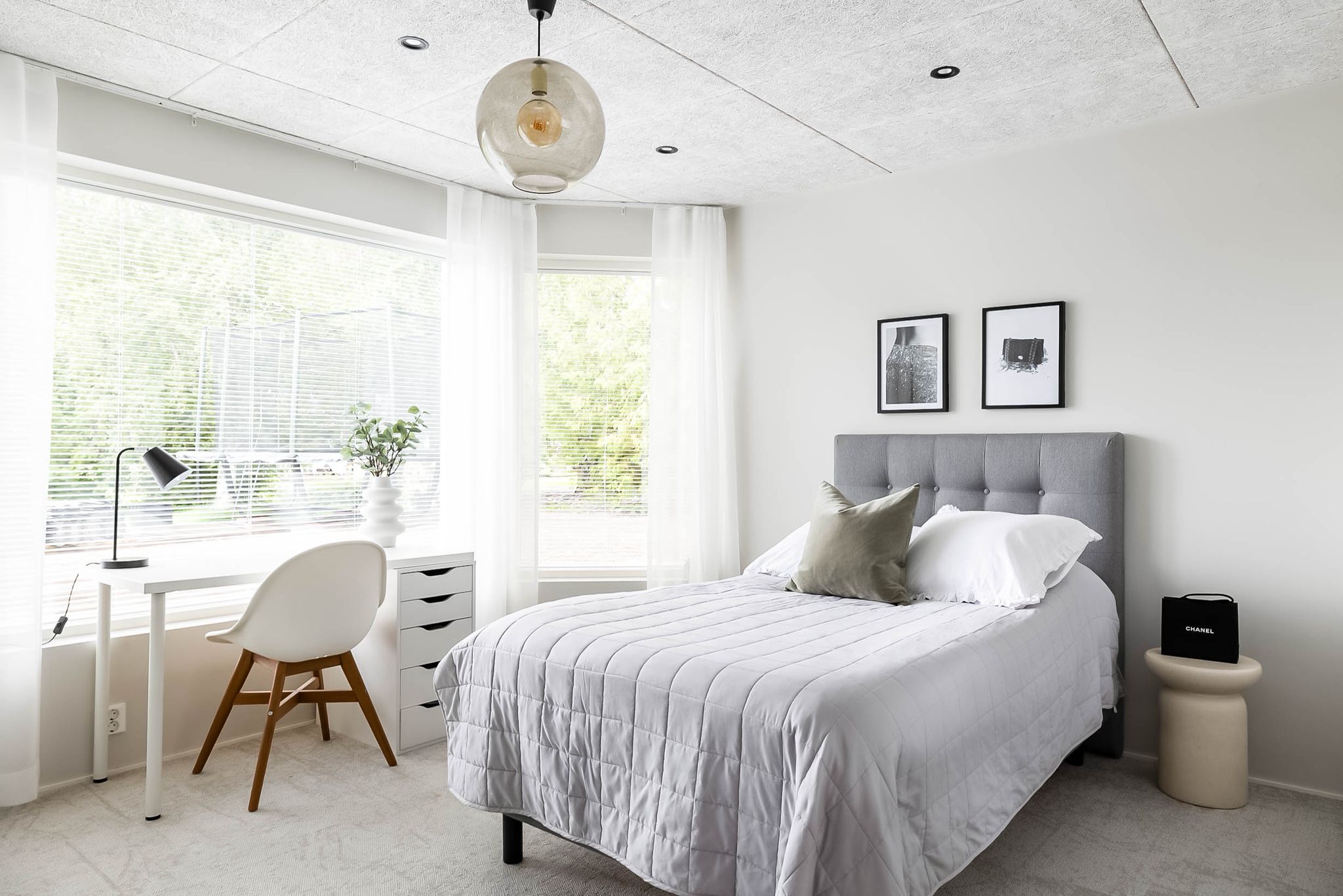 Bedroom in layered whites with a grey headboard, framed prints and a small workspace
