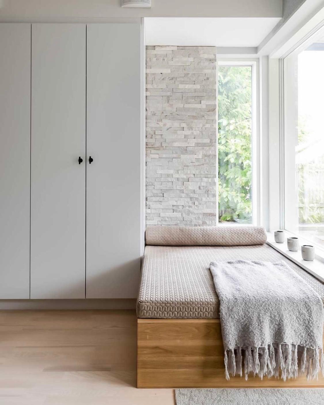 Bedroom corner with a window bench, white brick wall and cabinetry