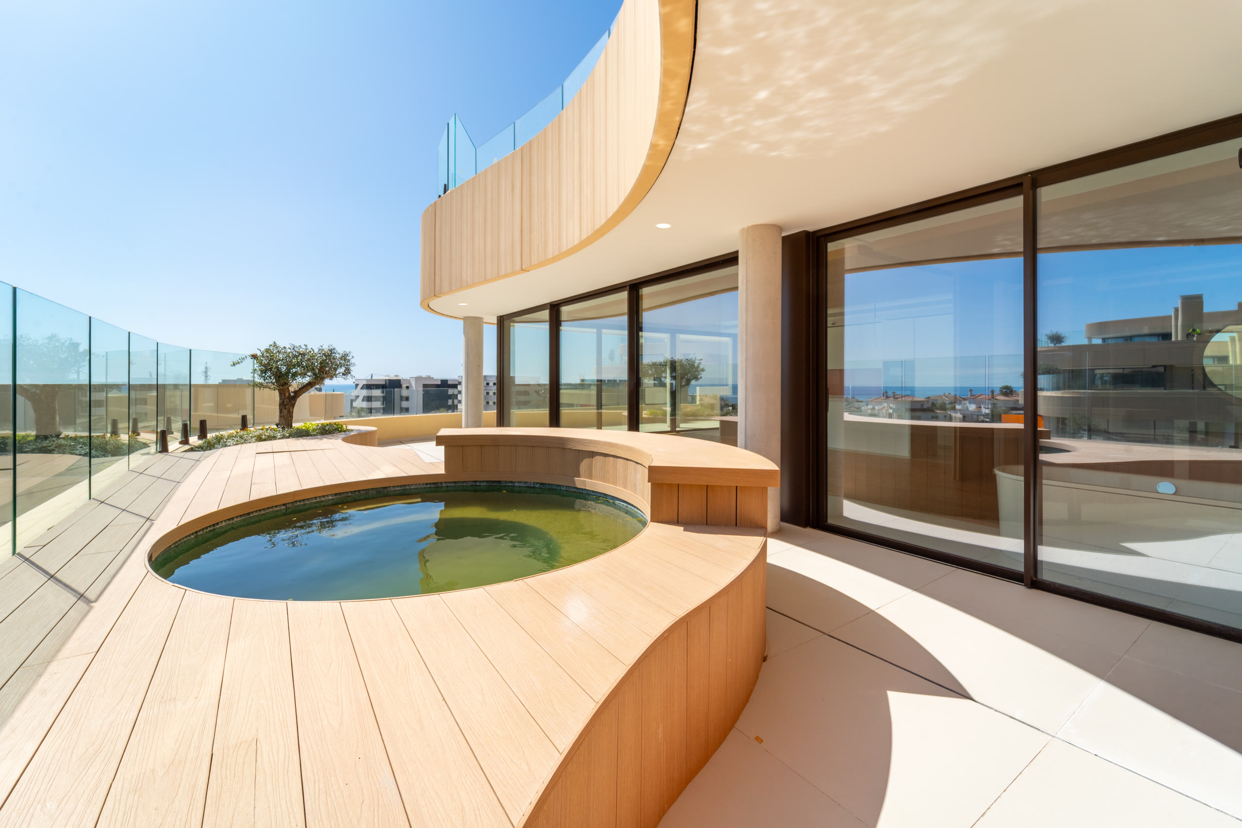 Curved terrace with built-in planters, olive trees and glass balustrades