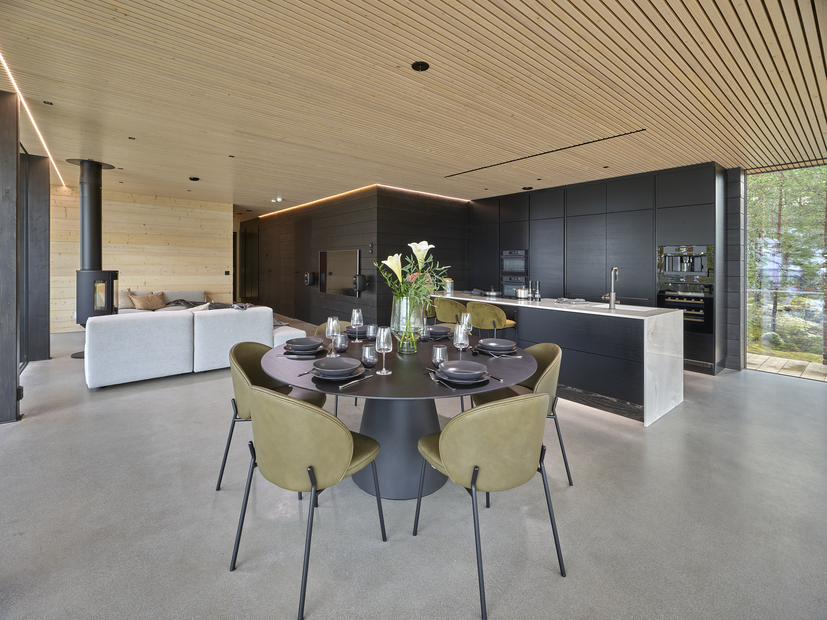 Living and dining area with a round dark table, olive-toned chairs and a black kitchen