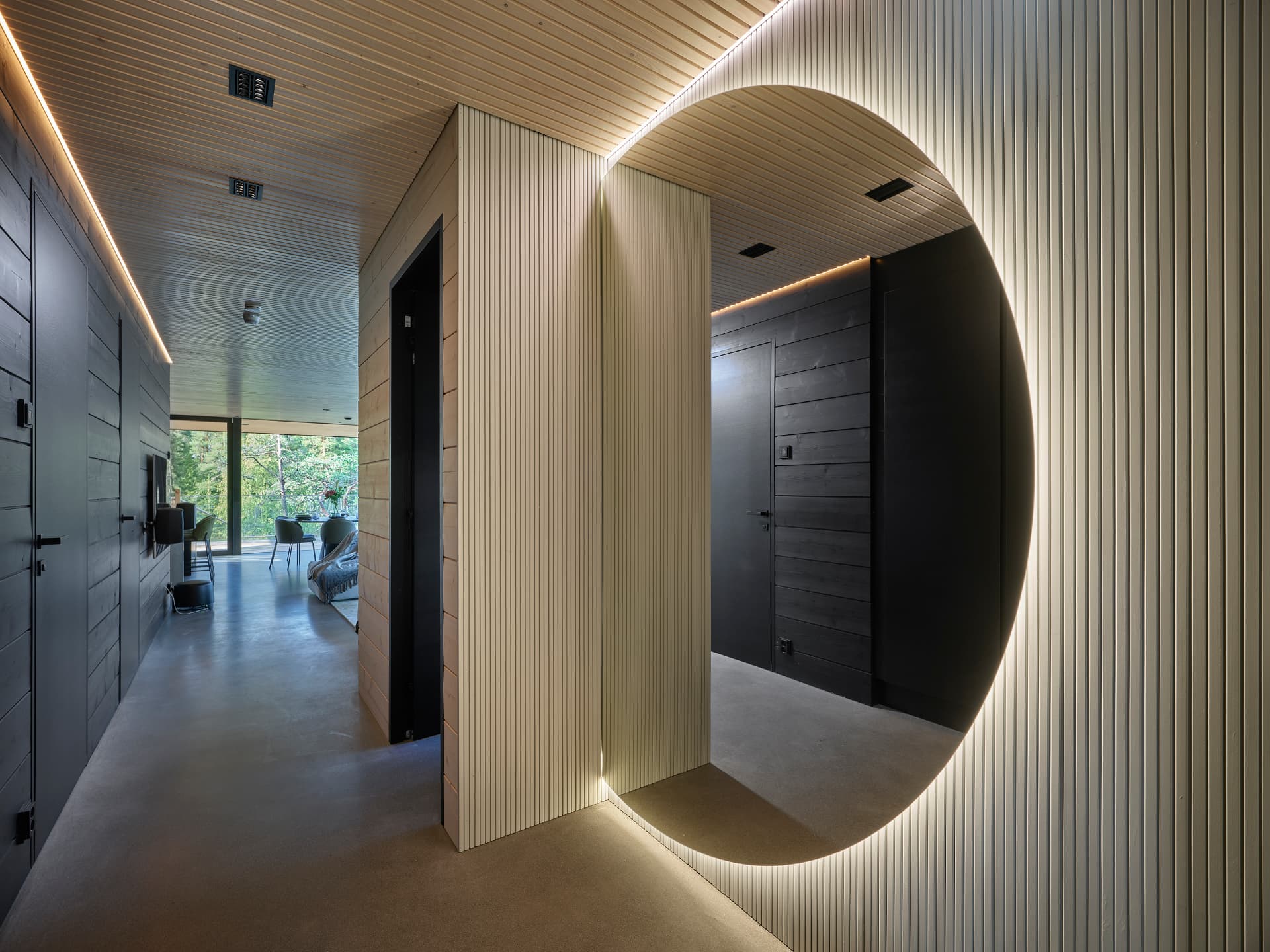 Timber-lined hallway with a large backlit round mirror and dark wood doors