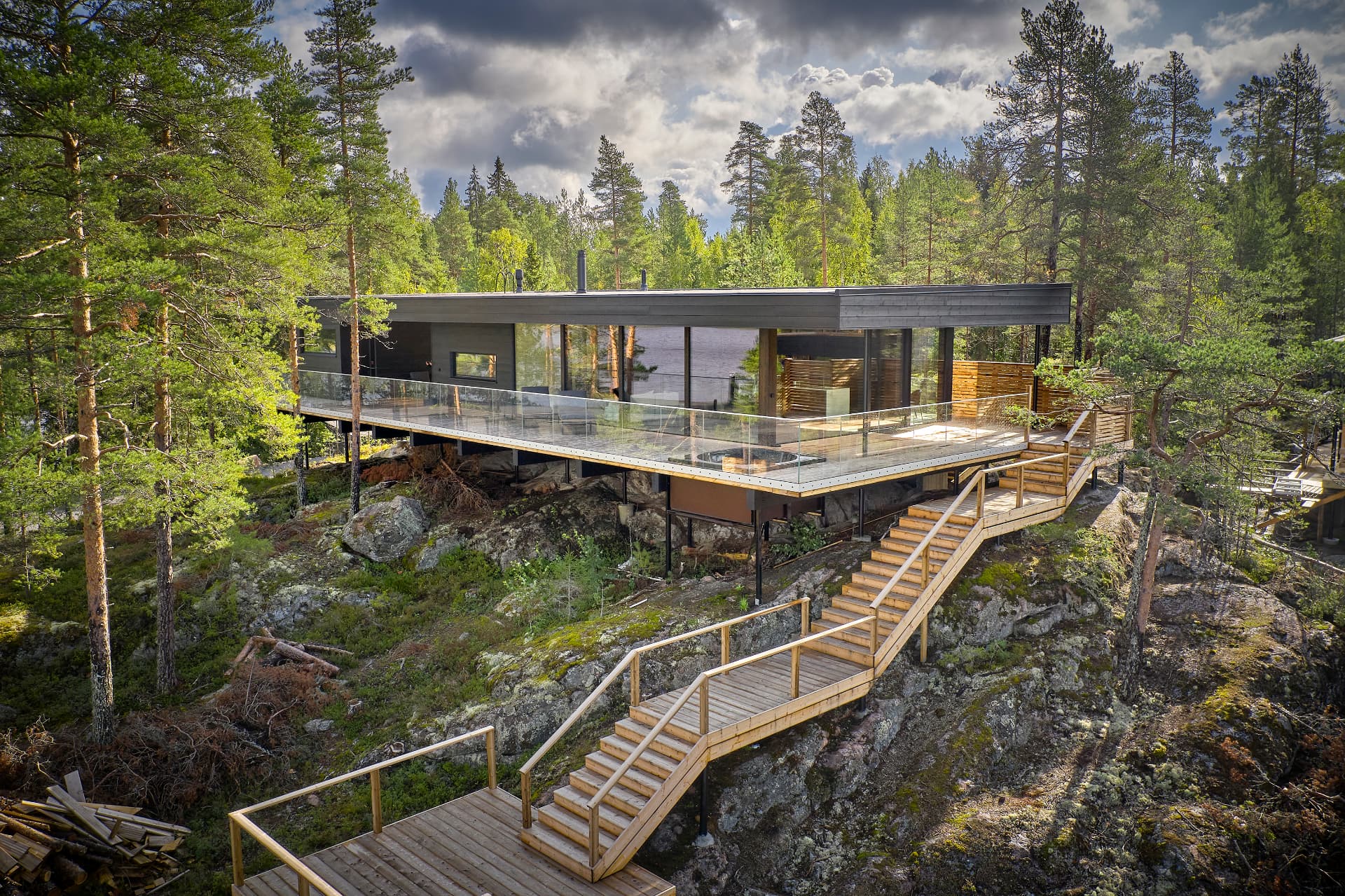Aerial view of a dark timber house on a rocky forest slope above the water