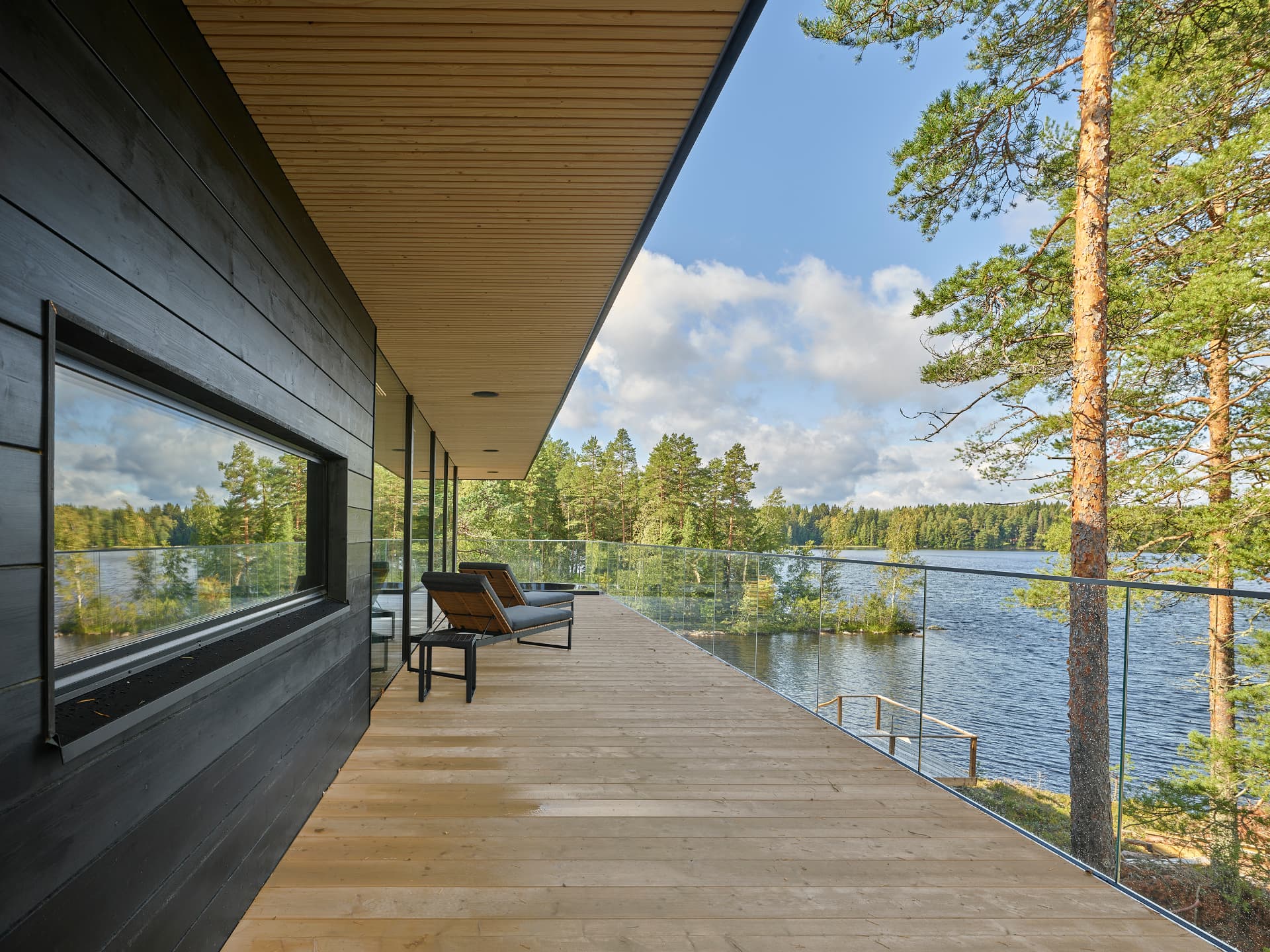 Covered terrace with timber decking, glass balustrade and a lake view through the pines