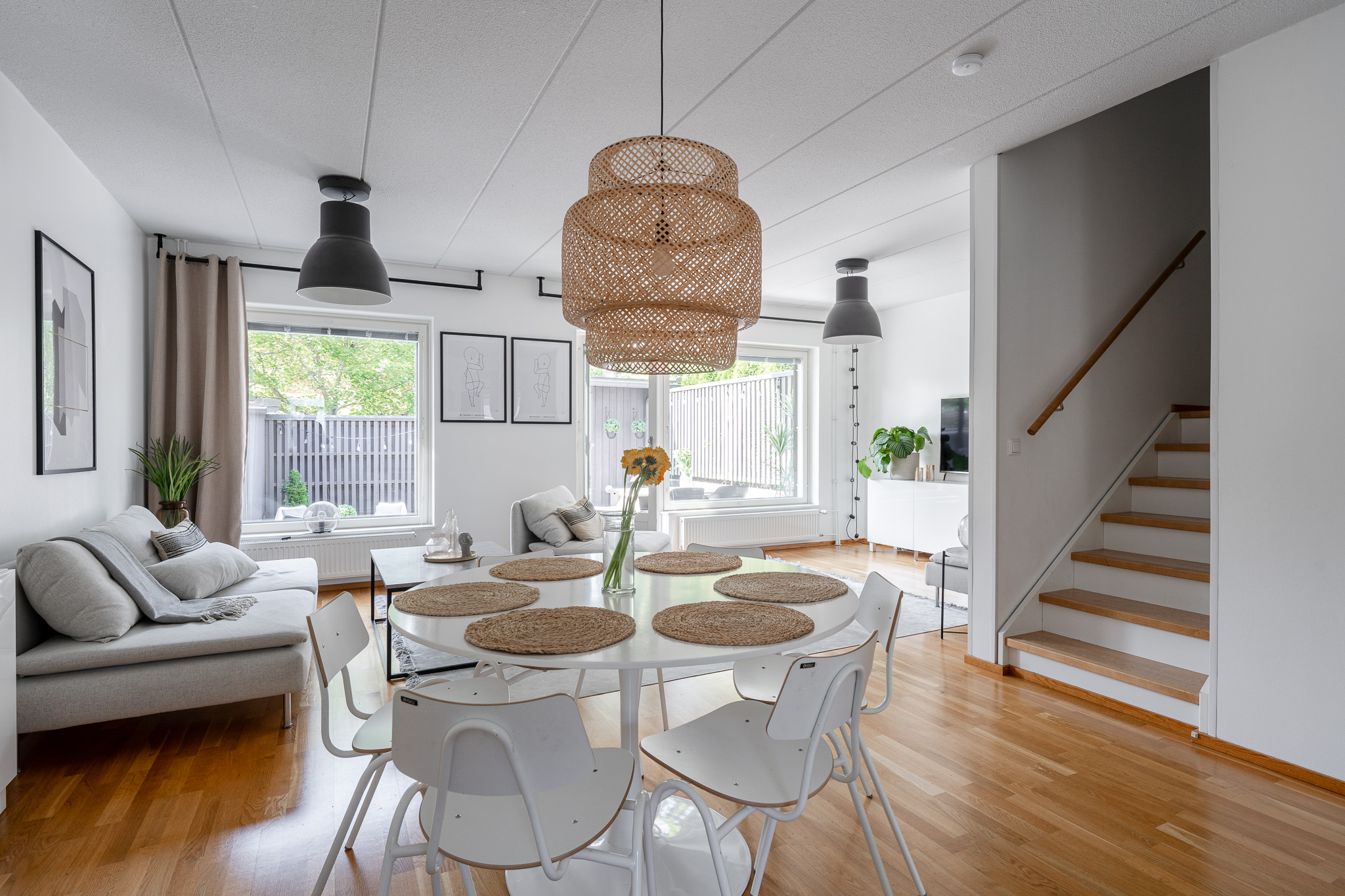 Open-plan living space with a dining table, rattan pendant light and a view towards the stairs