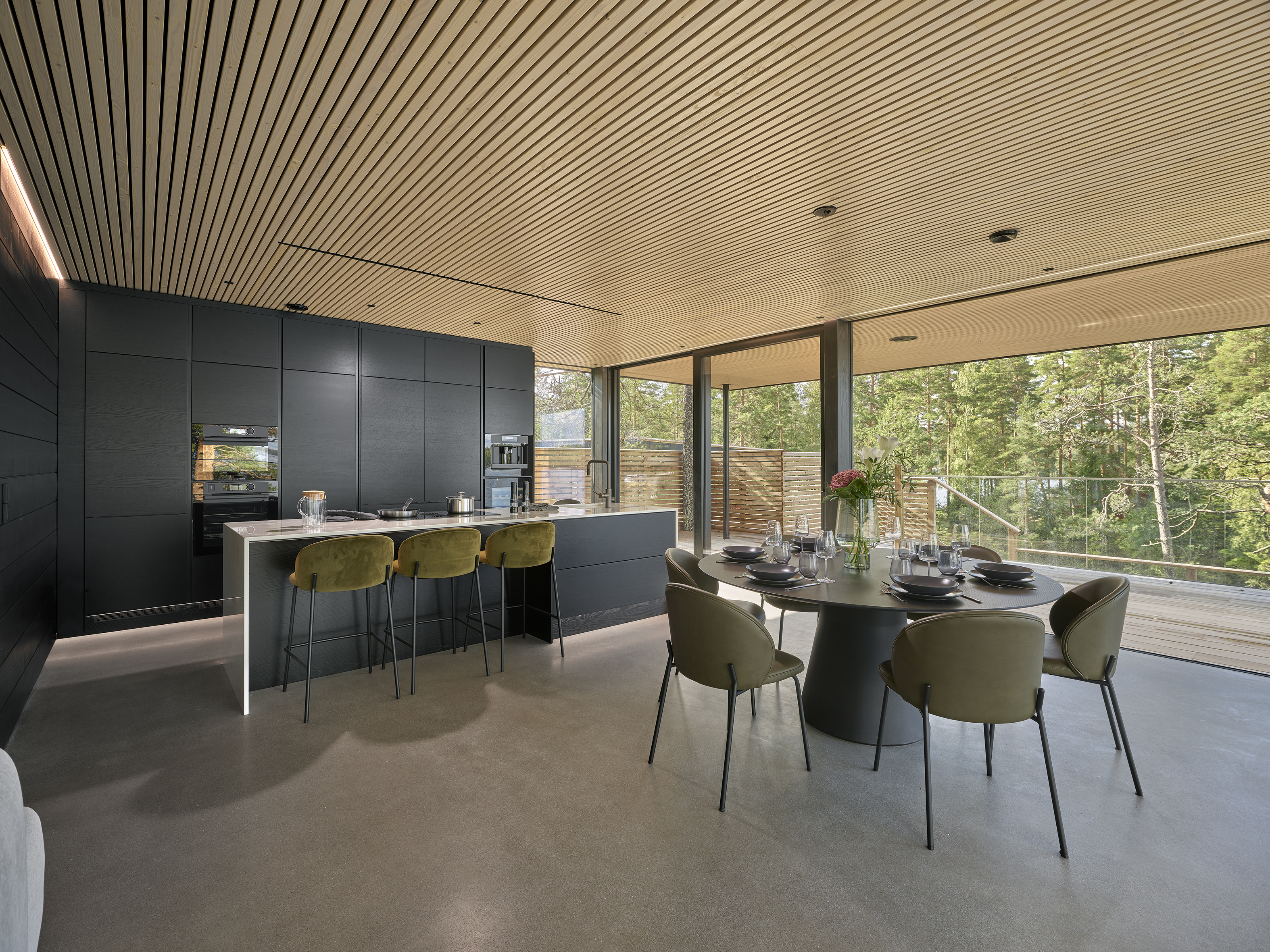 Open kitchen and dining space with a slatted timber ceiling and full-height windows onto the pines
