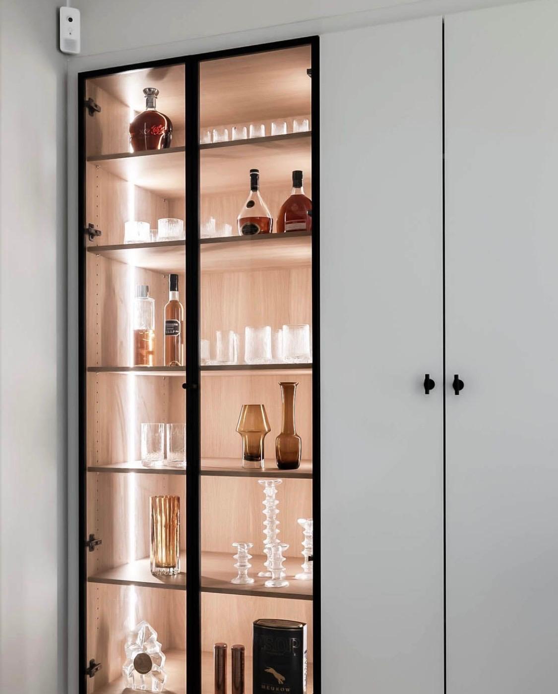 Backlit glass cabinet displaying glassware and ceramics in warm light