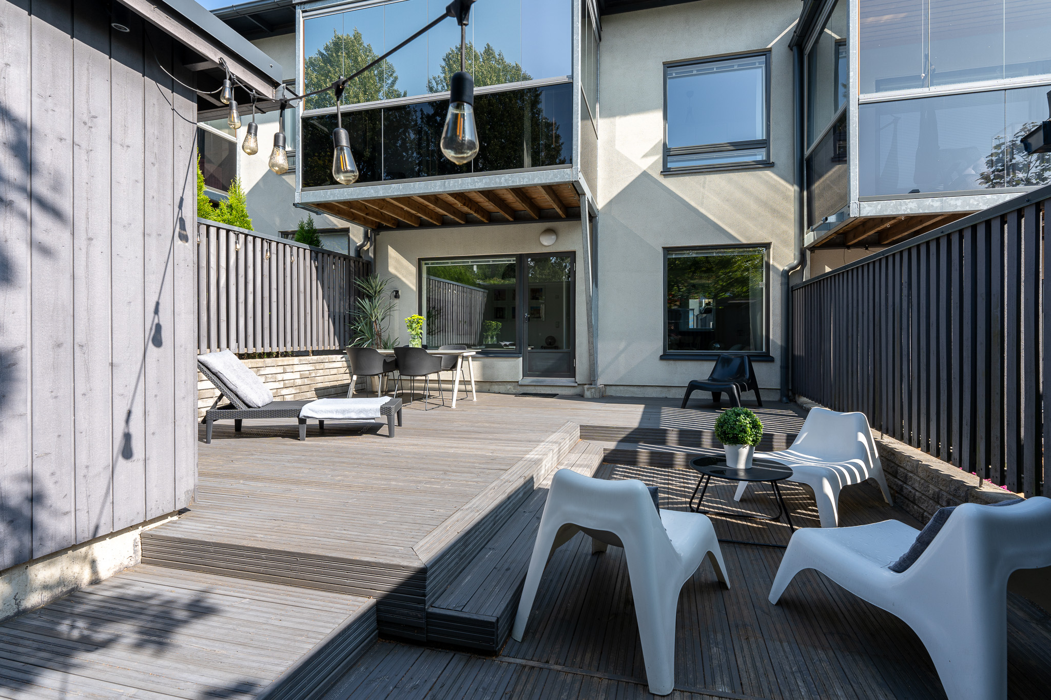 Wide sunlit terrace with lounge chairs and outdoor dining beneath a timber-clad overhang