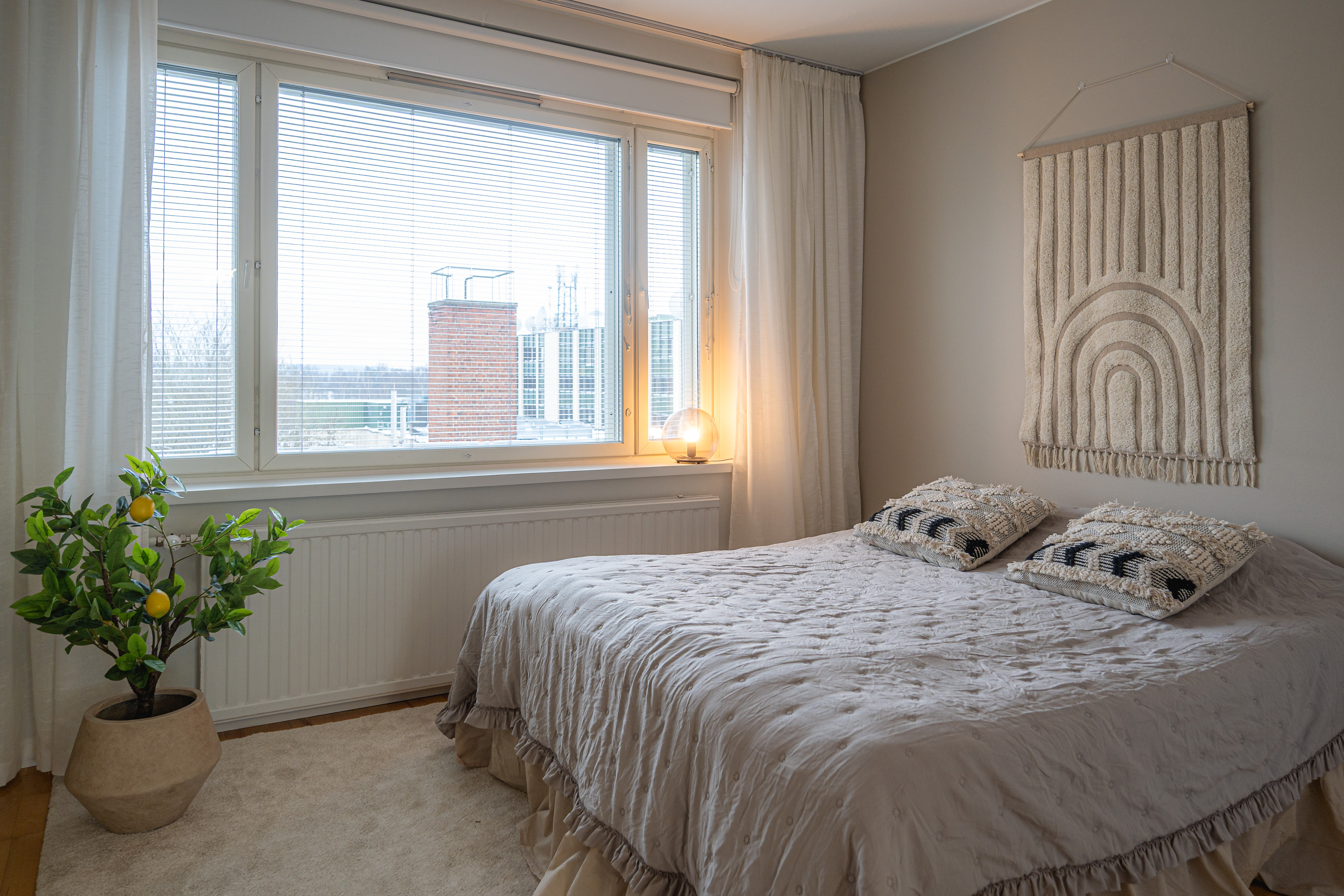 Bedroom in calm neutrals with a macramé wall hanging and soft linen bedding