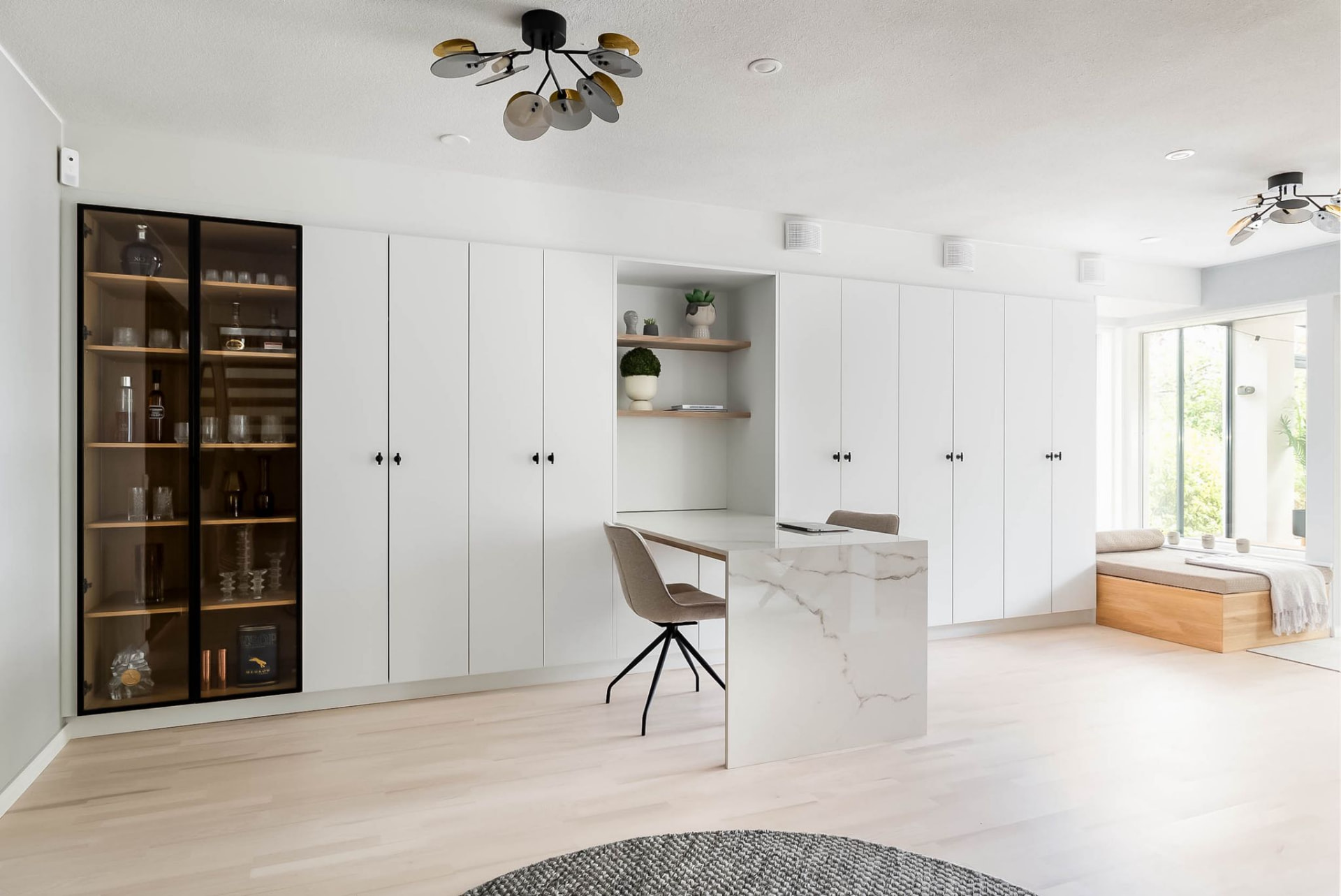 Bright room with full-height white cabinetry, glass display unit and marble desk