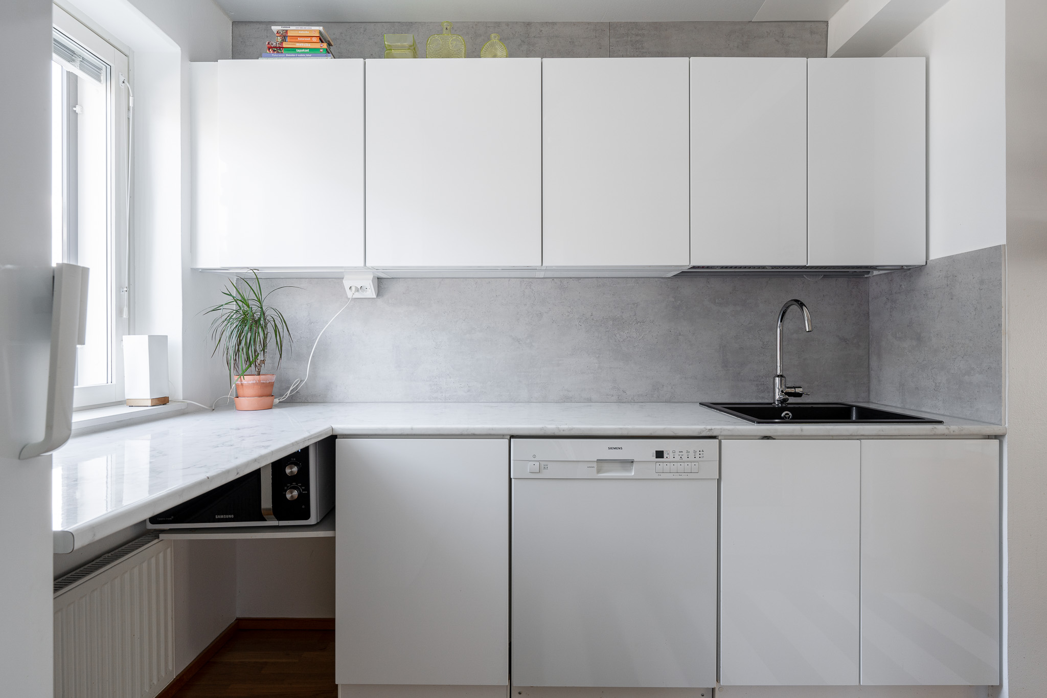Compact all-white kitchen with marble-look worktop and a window above the sink